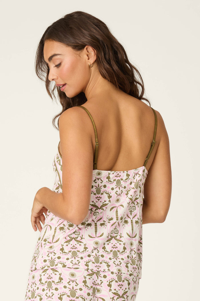 A woman with long brown hair looks over her shoulder in the P.J. Salvage Déjà Vu Dreams Tiki Time Camisole, featuring olive green straps and a pink floral and leaf design on a light background.