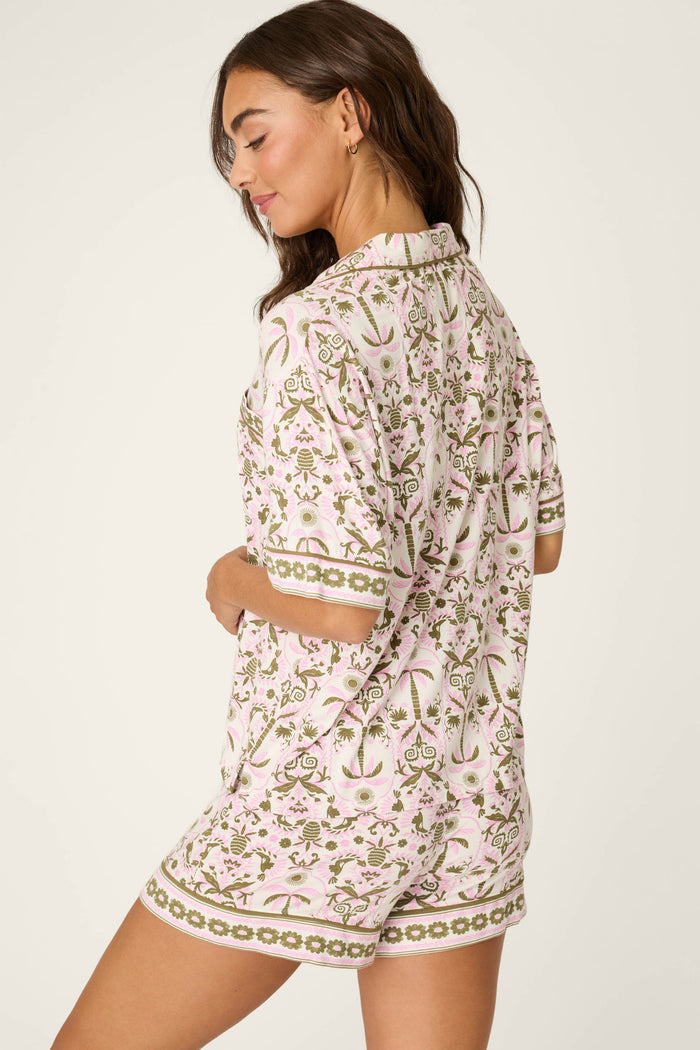 Woman with long brown hair, facing sideways and looking down, wears the P.J. Salvage Déjà Vu Dreams Tiki Time Short Sleeve Top against a neutral background.