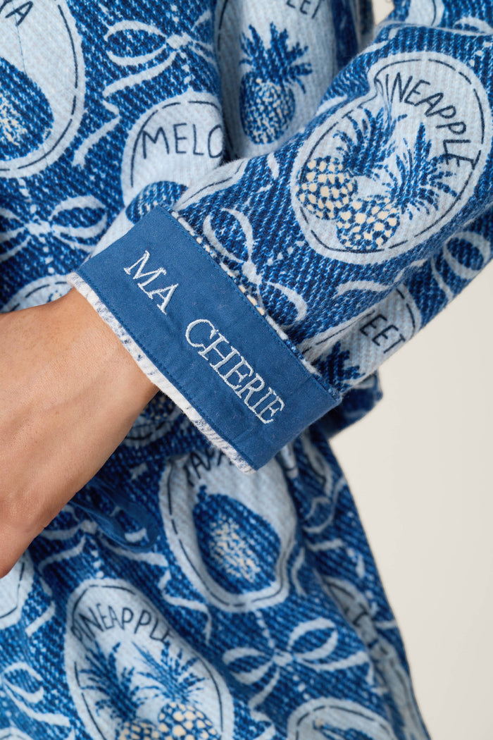 A close-up of the Fruit Medley Print 3-Piece Short Flannel PJ Set by P.J. Salvage shows a blue patterned sleeve featuring pineapples, the words "pineapple" and "melon," and a cuff embroidered with "MA CHÉRIE" in white.