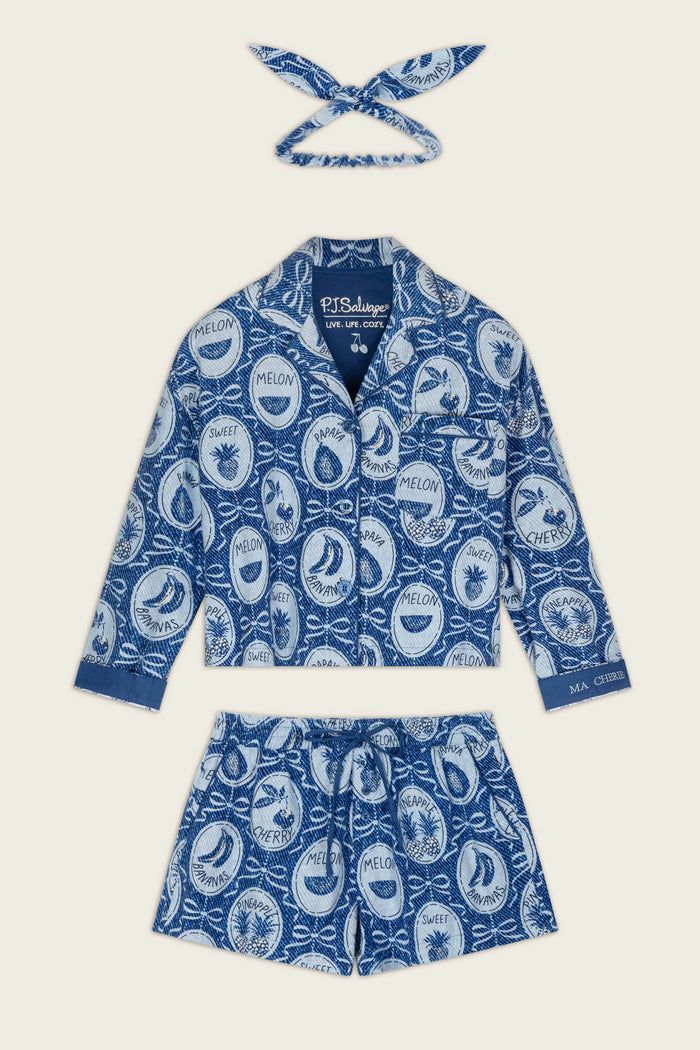 The Fruit Medley Print 3-Piece Short Flannel PJ Set by P.J. Salvage features a blue and white pajama set adorned with playful circular fruit labels and names like melon, banana, and cherimoya. This set includes a collared button-up shirt, drawstring shorts, and a matching headband.