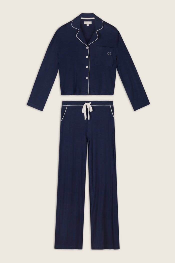 The Soiree Dreams Deep Navy Long Sleeve PJ Set by P.J. Salvage, featuring white piping, includes a button-up top with a front pocket and matching drawstring pants, displayed flat on a light background.