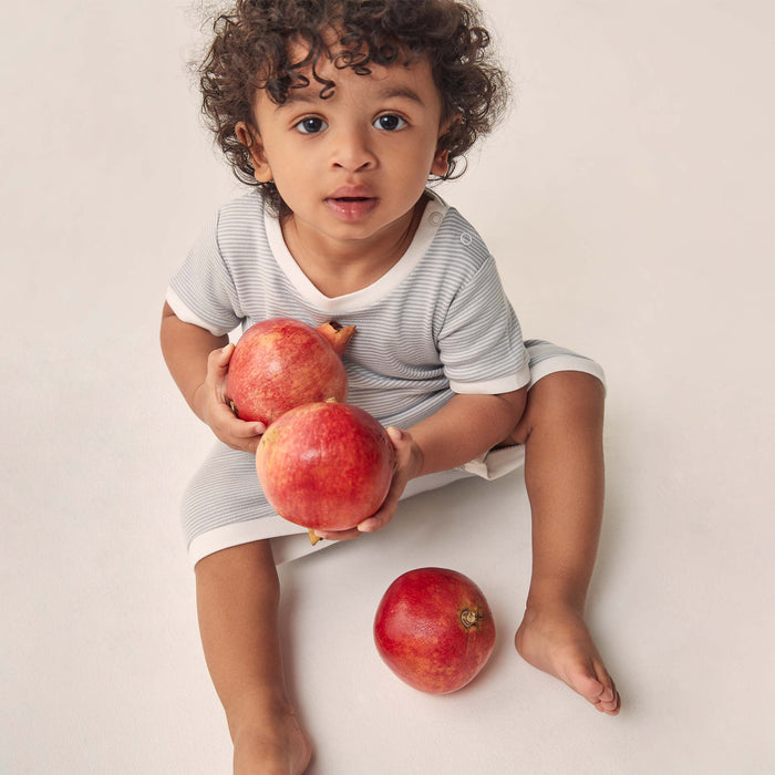 toddler holding pomgranades wearing a summer sleepsuit