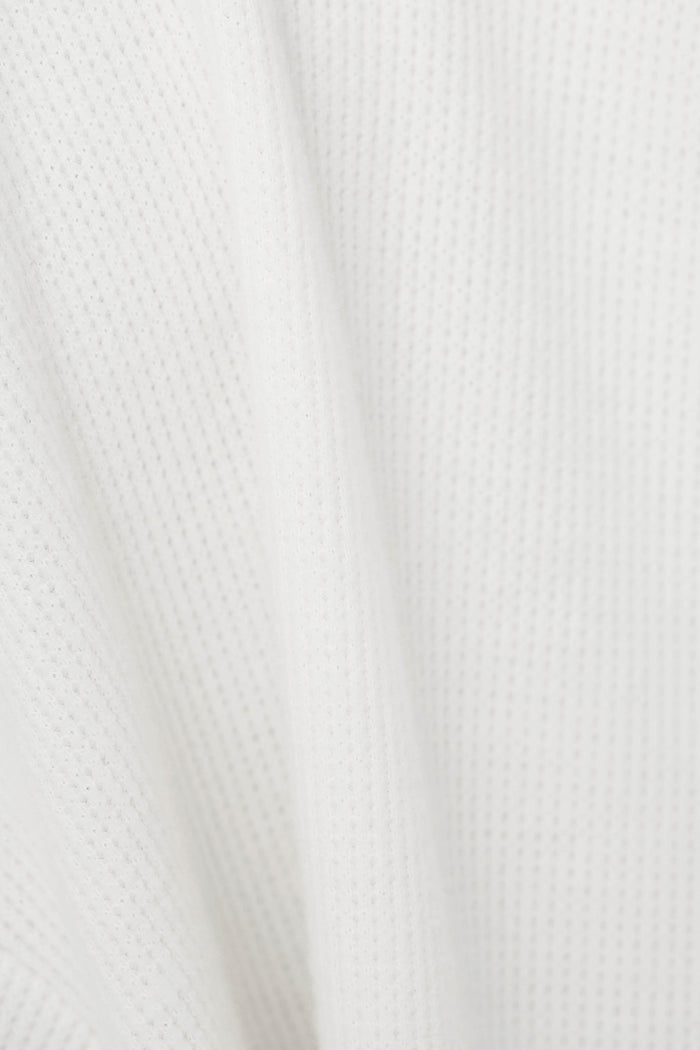 Close-up of a white textured fabric with a fine waffle pattern and soft folds.
